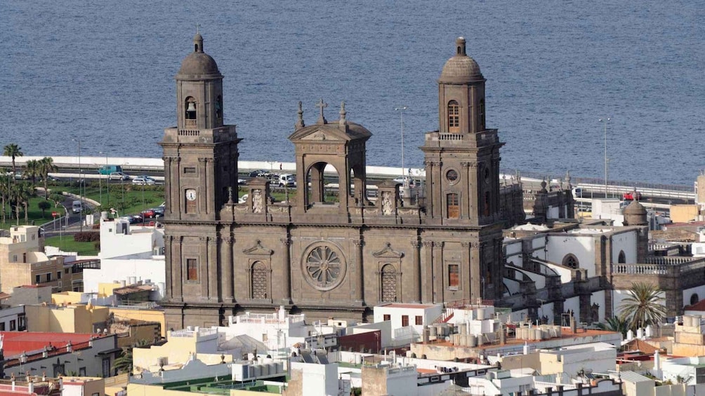 A historic church with two bell towers and a large central dome, surrounded by urban buildings and a coastline. 3