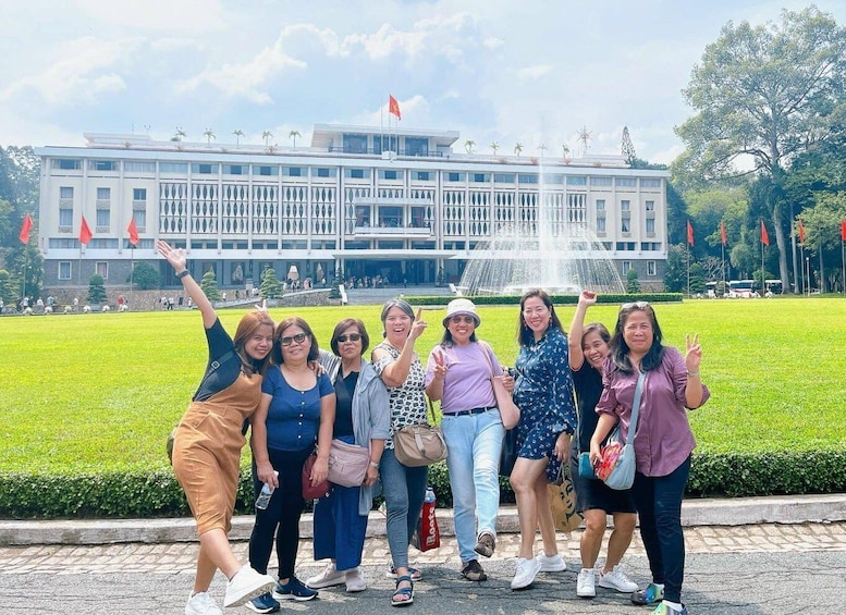 A group of people posing in front of a large building with a fountain and palm trees in the background. 1