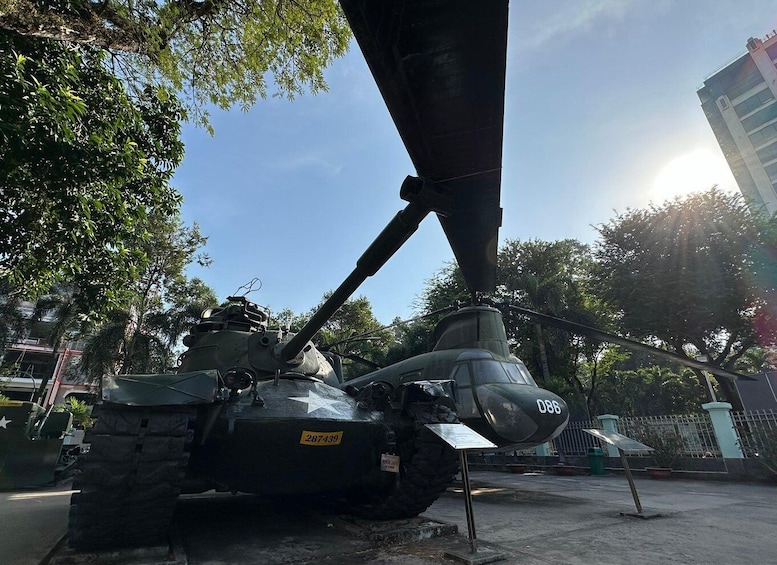 A military vehicle with a mounted cannon, parked outdoors with trees and a building in the background. 3
