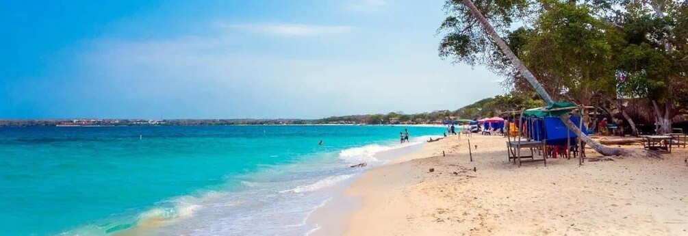 A beach with clear turquoise water, a sandy shore, and a few people swimming. 4