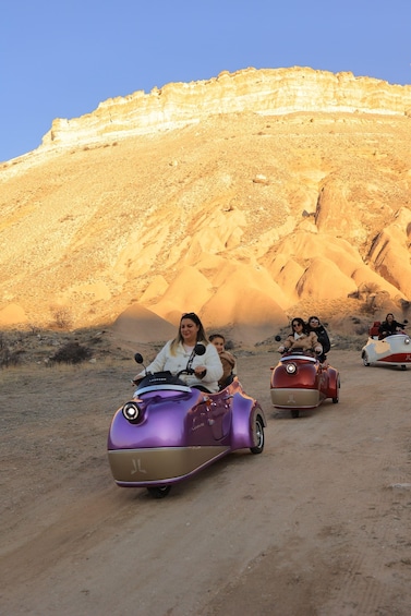 People riding vintage cars on a desert road with a rocky backdrop. 2
