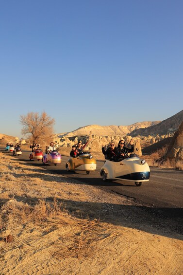 People in vintage cars driving on a road in a desert landscape. 3