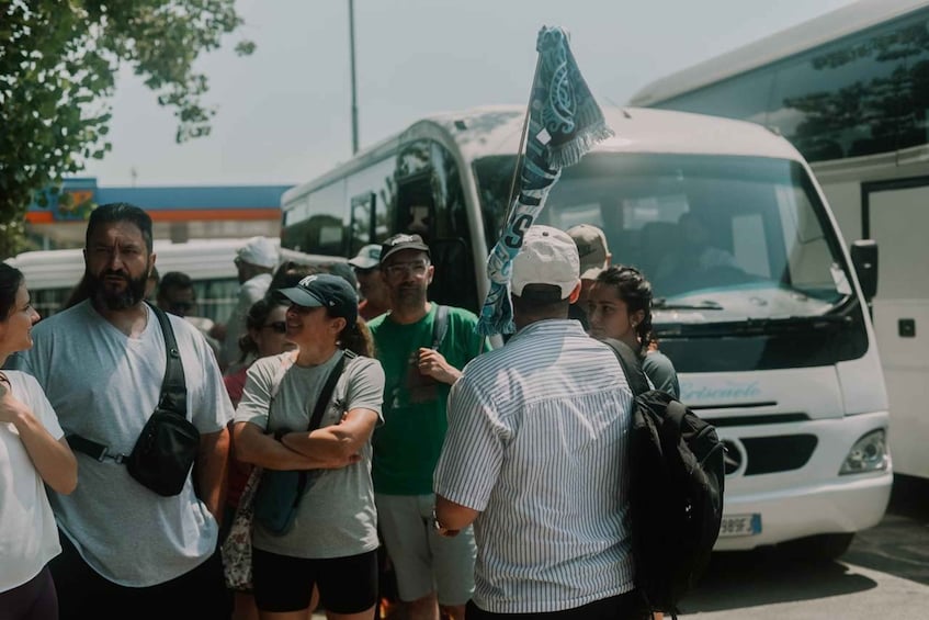 A group of people standing in a line, some with backpacks, in front of a white van with a blue and white design. 4
