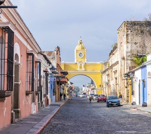 A cobblestone street with historic buildings, a yellow archway, and a clock tower. 3