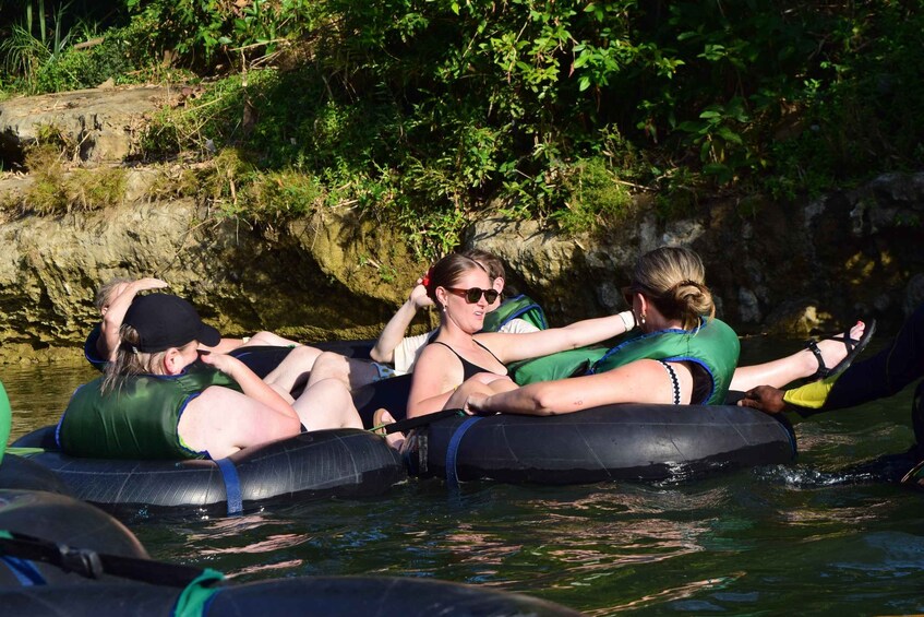 Menschen treiben auf Wasserschläuchen in einem Fluss, umgeben von viel Grün. 2