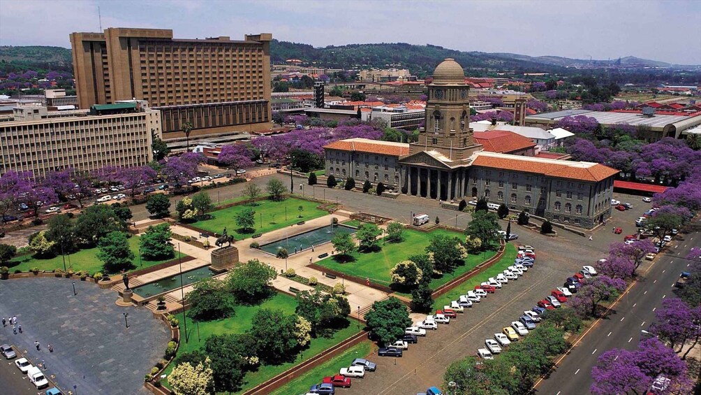 A cityscape with a large building, a central plaza with a statue, and a parking lot. 4