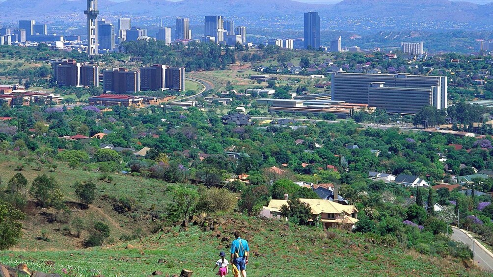 A cityscape with a mix of high-rise buildings and greenery, a winding road, and a person walking with a child. 2