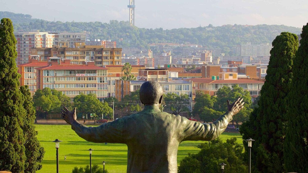A statue of a man with outstretched arms in a park with buildings in the background. 5