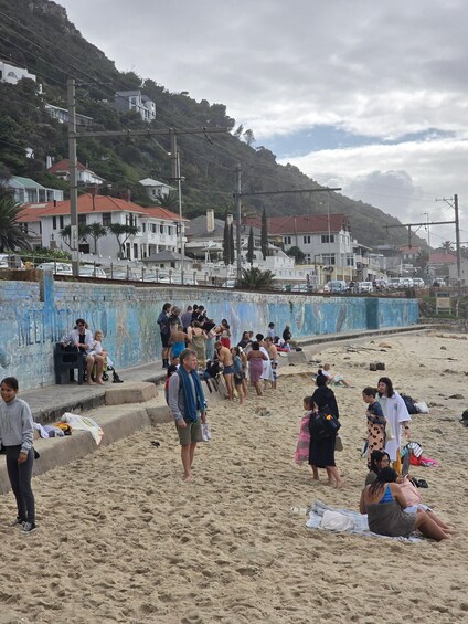 Une plage où l’on voit des gens se promener et s’asseoir, un mur bleu et des maisons en arrière-plan. 3