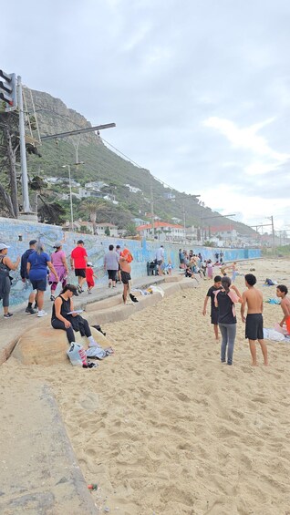 Une plage où l’on voit des gens assis et debout sur les marches, une plage de sable, et des maisons en arrière-plan. 2