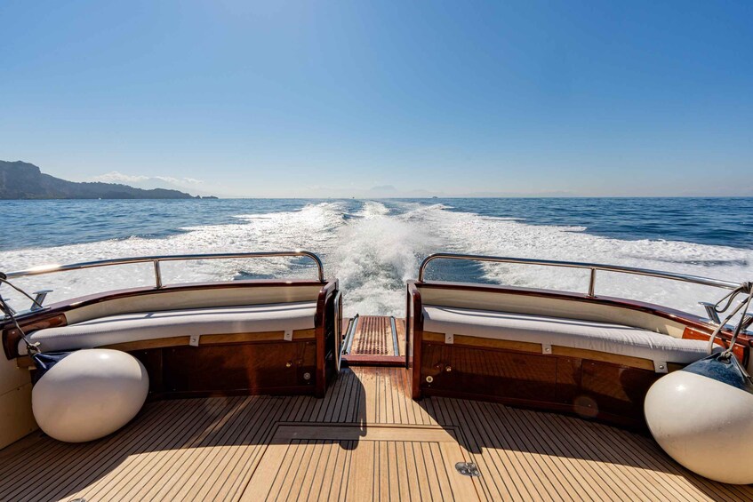 A boat's deck with wooden flooring and two white buoys, heading towards a calm sea with a clear sky. 5