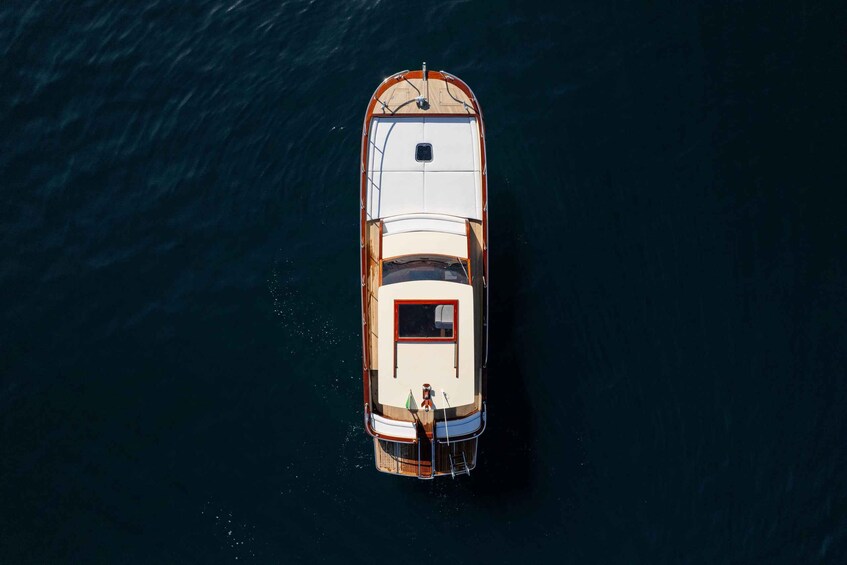 An aerial view of a boat with a white deck and a red cabin, anchored in calm waters. 1