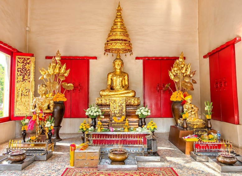 A golden Buddha statue in a temple with red doors and various offerings. 3