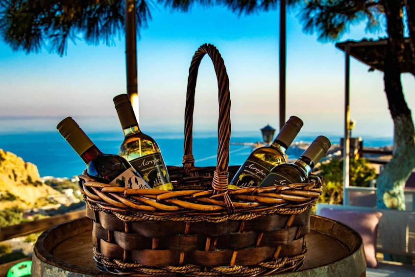 A wicker basket filled with bottles of Acropoli wine, set against a scenic coastal backdrop. 2