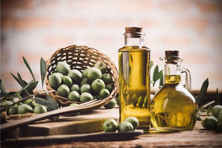 Olive oil bottles, a basket of green olives, and a wooden cutting board. 4