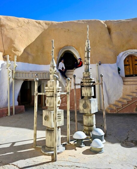 A desert-themed architectural structure with a café entrance, a person sitting on a ledge, and decorative elements resembling a futuristic cityscape. 4