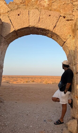 A man standing in a desert landscape, looking through an ancient stone archway. 5