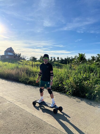 A person on a hoverboard on a paved path with greenery and a house in the background. 1