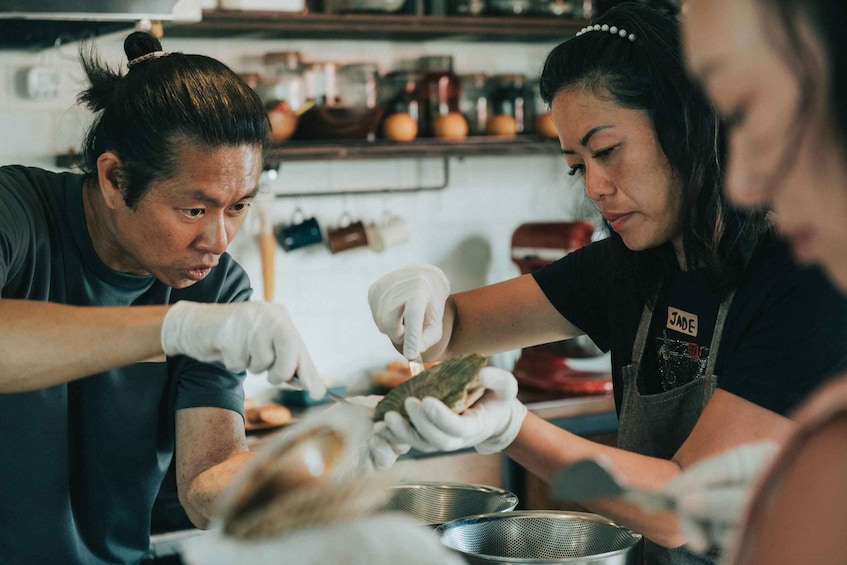Two people preparing food, wearing gloves and aprons, in a kitchen setting. 1