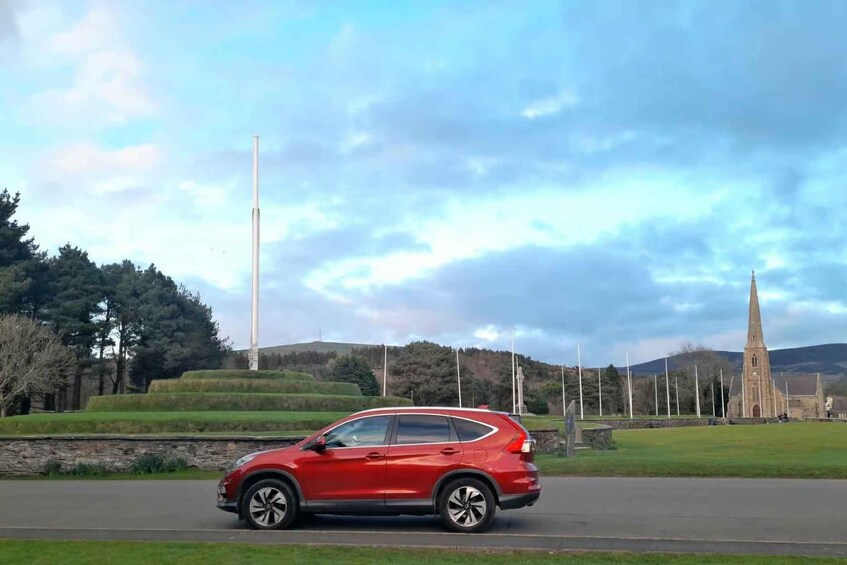A red car on a road with a church and a tower in the background. 5