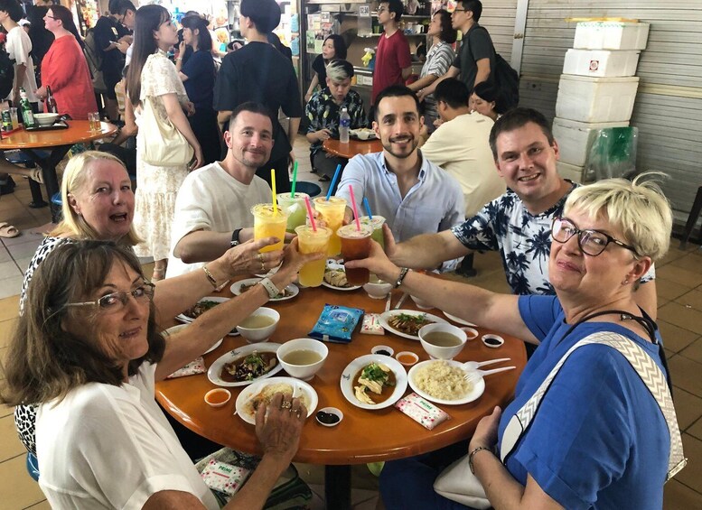 A group of people toasting with drinks at a round table in a crowded indoor setting. 3