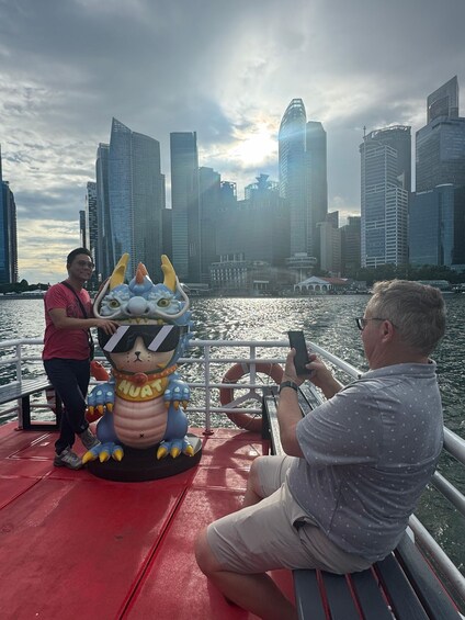 A person taking a photo of a large inflatable character on a boat with a city skyline in the background. 1