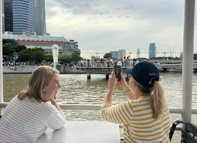 Two people on a boat, one taking a photo, with a cityscape and a bridge in the background. 5