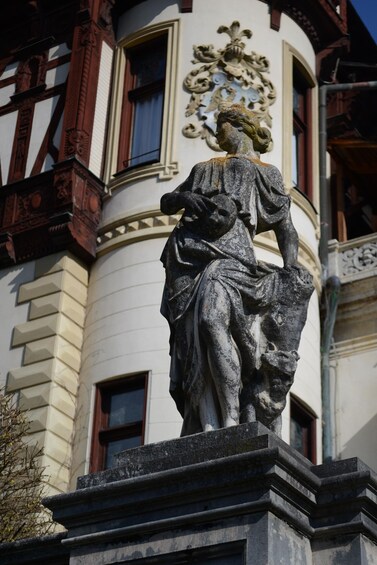 A statue of a woman holding a child on a pedestal in front of a building with a decorative crest. 2