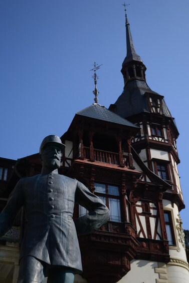 A statue of a man in a suit and hat in front of a historic building with a spire. 4