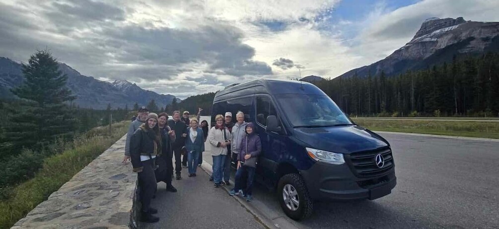 A group of people standing next to a black van on a road with mountains in the background. 5
