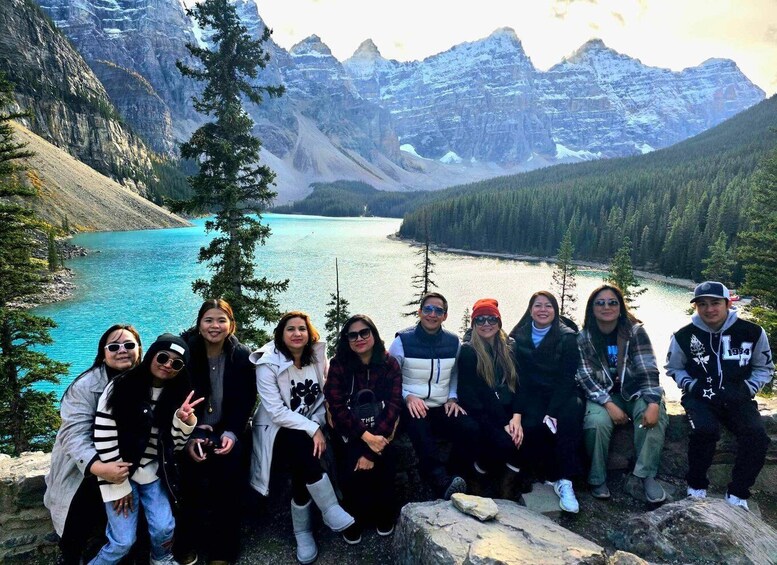 A group of people posing in front of a mountain lake with snow-capped peaks in the background. 4