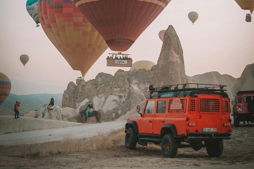 A red off-road vehicle, hot air balloons, and rocky terrain. 3