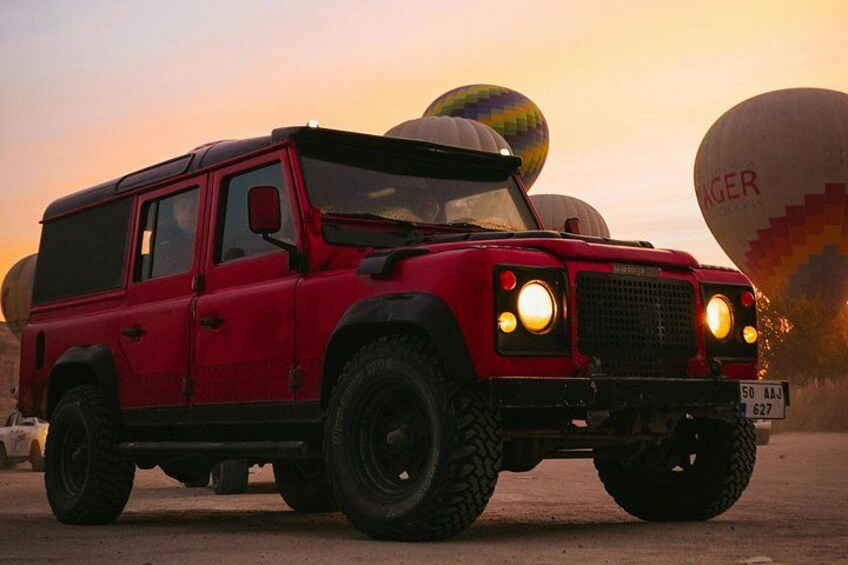 A red off-road vehicle with large tires parked in front of hot air balloons. 4