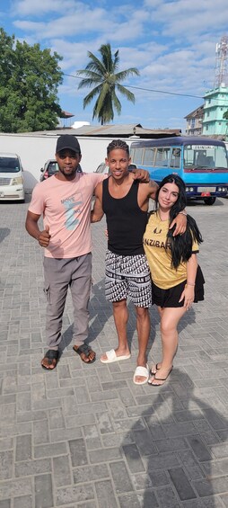 Three people standing on a paved area with a bus and a building in the background. 3