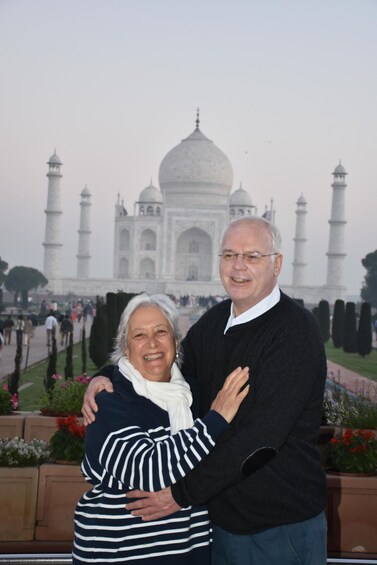Two people embracing in front of a large white monument with domes and minarets. 2