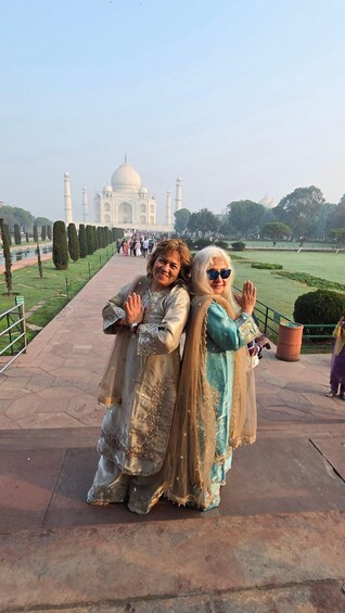 Two people posing in front of the Taj Mahal, with a pathway and trees in the background. 3