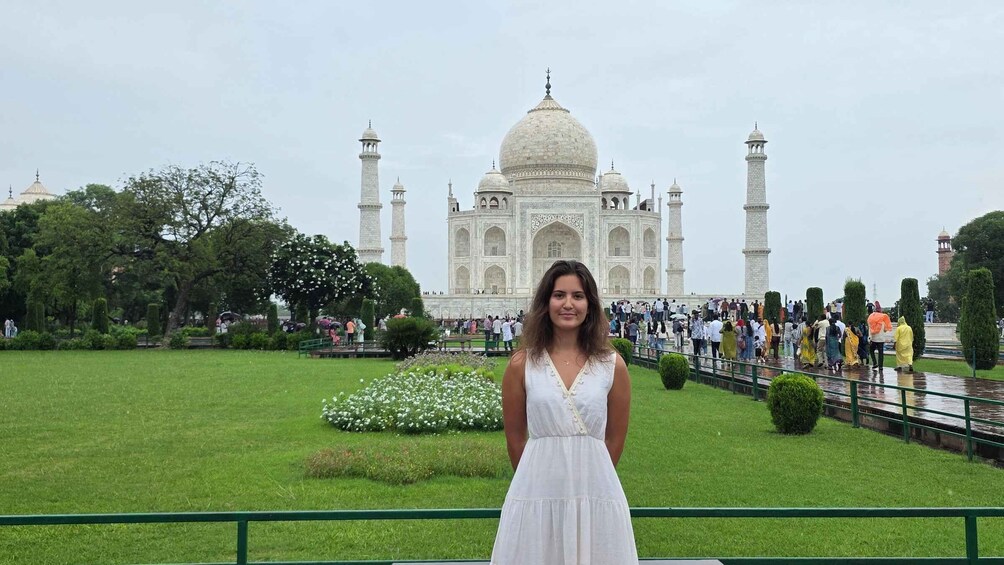 A woman in a white dress standing in front of the Taj Mahal with a crowd in the background. 2