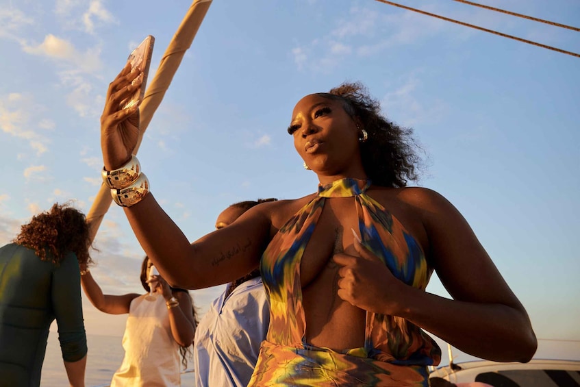 A person wearing a colorful dress, holding a phone, and standing on a boat. 1