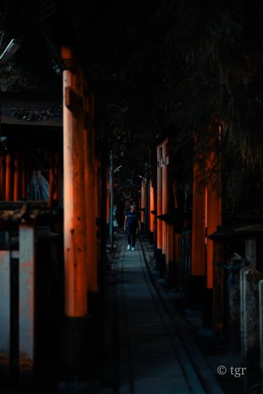 A person walking through a corridor lined with orange torii gates. 5