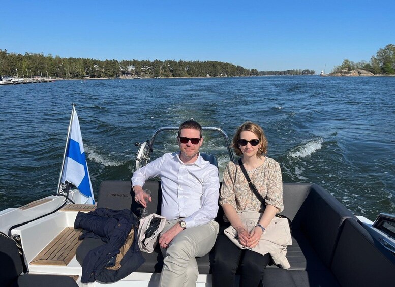 Two people on a boat with a flag, water, and a distant shoreline. 1