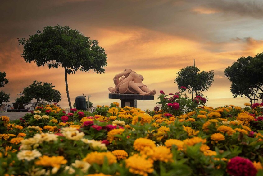Une sculpture représentant deux personnages qui s’enlacent, entourés de fleurs aux couleurs vives, avec des arbres et un coucher de soleil en arrière-plan. 5