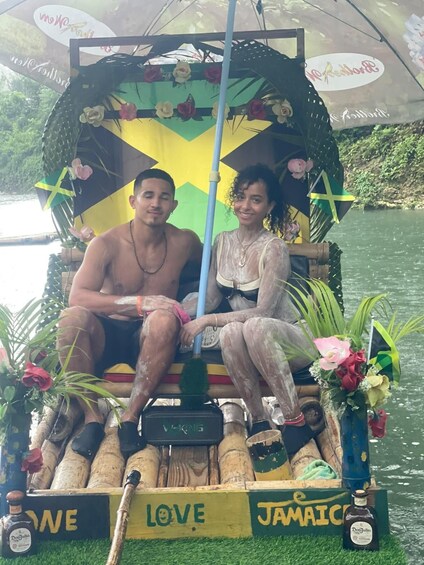 Two people on a boat decorated with flowers and flags, with 'LOVE' and 'JAMAICA' written on it. 2