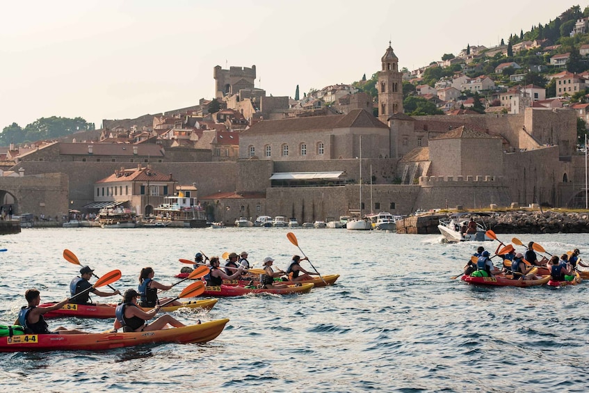 A group of people in colorful kayaks paddling on a river in front of a historic city with a prominent castle. 5