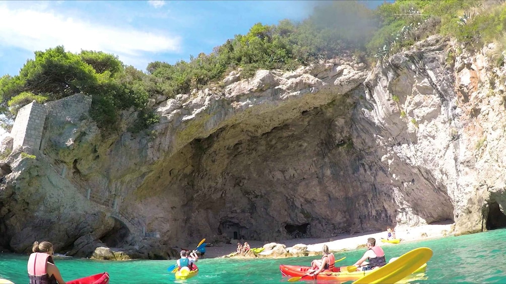 People kayaking in a cove with rocky cliffs and greenery in the background. 3