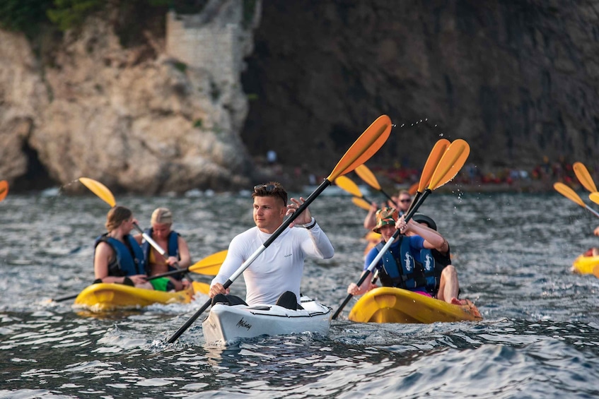 People kayaking on a calm body of water with rocky cliffs in the background. 1
