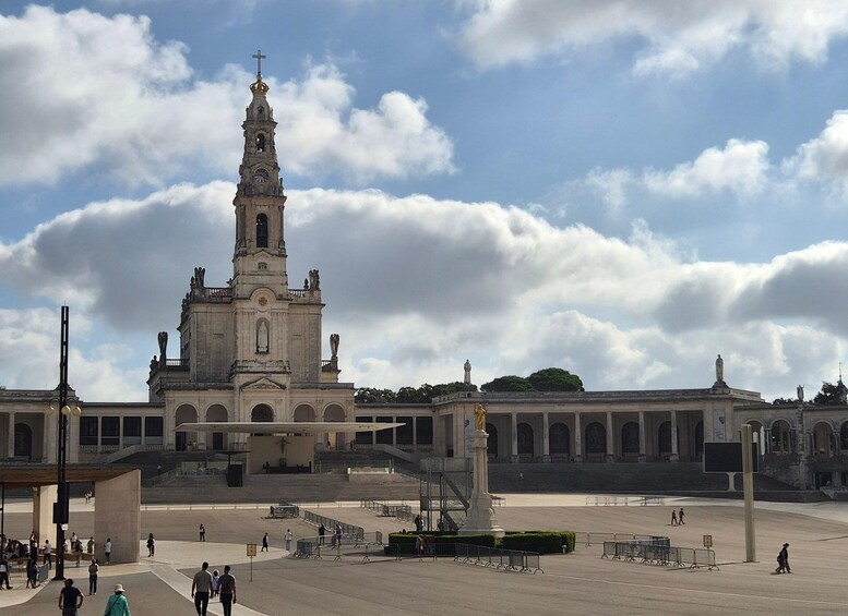 Un edificio storico con un'alta torre e statue, circondato da una piazza aperta e persone che passeggiano. 1