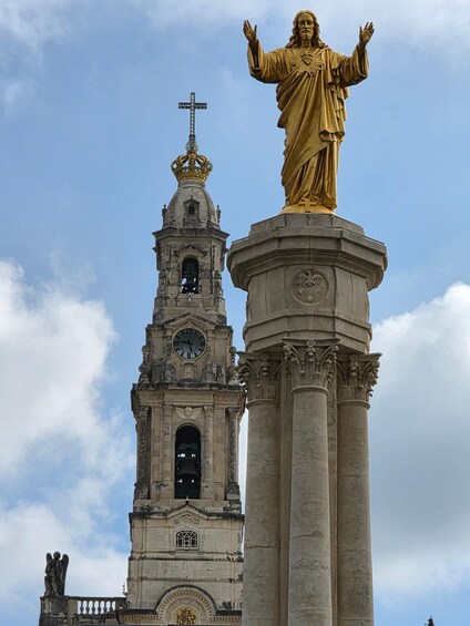Una statua dorata sulla sommità di una colonna, una torre dell'orologio con una croce e una campana. 2