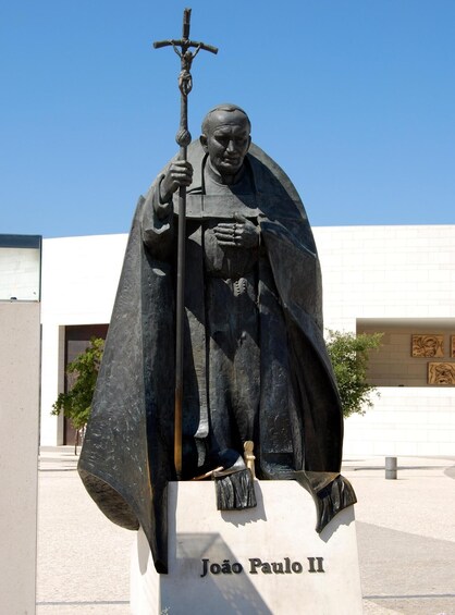 Una statua di un uomo che tiene una croce, con l'iscrizione "João Paulo II", di fronte a un edificio. 5