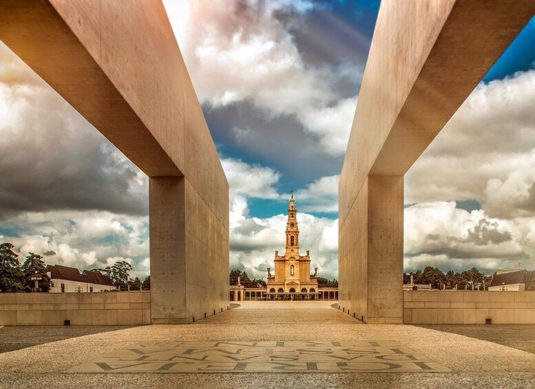 Una cattedrale con un'alta torre sotto un cielo nuvoloso, vista da una piazza con grandi strutture in cemento che incorniciano l'immagine. 3