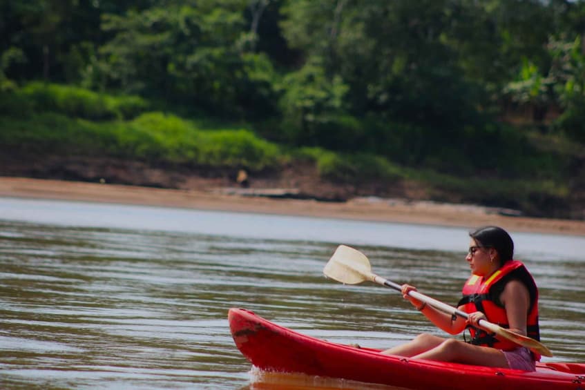 A person in a red kayak on a calm river, wearing a life jacket and holding a paddle. 2